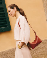Woman in profile with a crossbody bag, standing near a wall and window