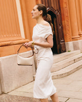 Person in a dress holding a handbag, standing outside a building with steps.