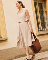 Woman walking down the street, wearing a skirt and sleeveless top, carrying a large tote.
