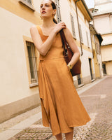 Person in sleeveless top and flowy skirt, holding a large bag, standing on a cobblestone street.