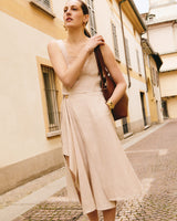 Person in sleeveless top and flowy skirt, holding a large bag, standing on a cobblestone street.