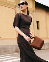 Person wearing sunglasses holding a bag, standing on a street.