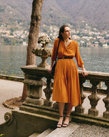 Person in a dress stands by a railing, overlooking a lake and hills.