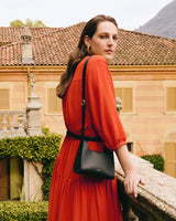 Woman in a dress by a balcony with a bag, villa in background.