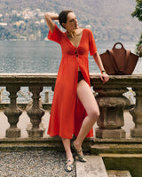 Person in a dress leaning on stone railing with a handbag nearby and lake in the background.