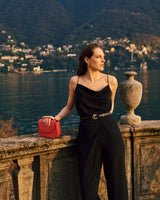 Person standing by a stone railing with a lake and mountains in the background.