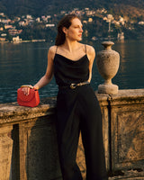 Person standing by a stone railing with a small bag, overlooking a lake and distant buildings.