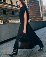 Person walking in city carrying a handbag wearing a sleeveless top, long skirt and knee-high boots