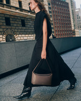 Person walking on city sidewalk carrying a handbag, wearing a skirt dress and boots.