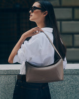 Person wearing sunglasses with shoulder bag and white shirt outdoors.