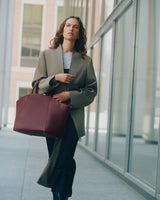 Person walking with large handbag in front of tall glass windows.