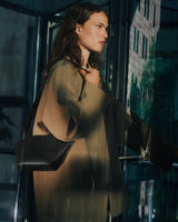 Person standing by glass door carrying a bag.