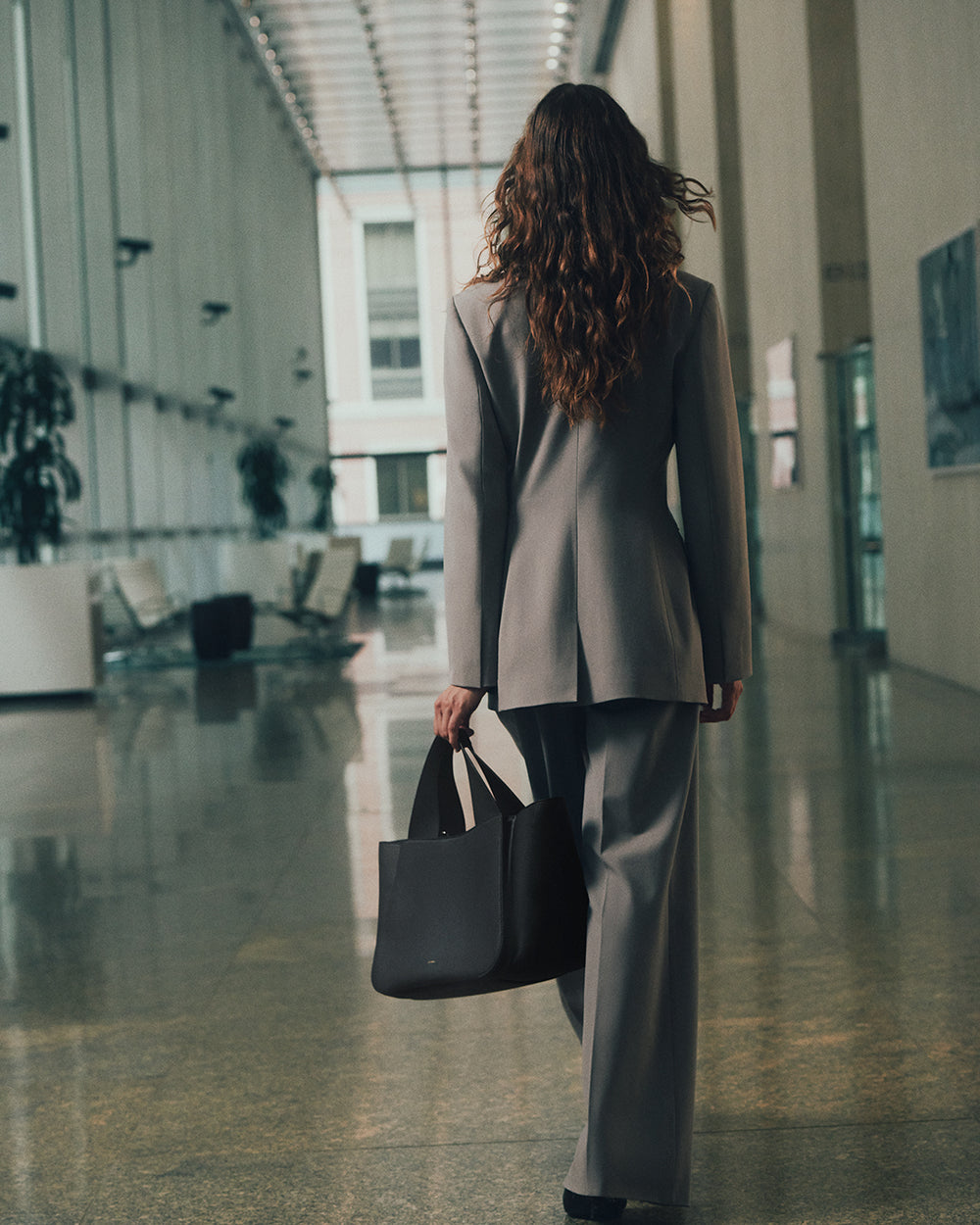 Wool Cinched Blazer Person in a suit walking indoors holding a bag.