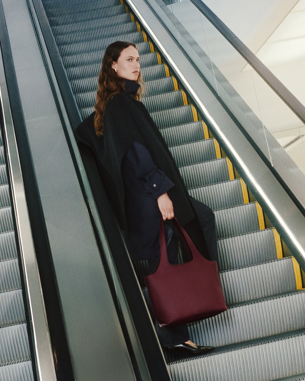 Person on escalator carrying a tote bag.