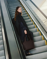 Person on escalator wearing a coat and holding a bag
