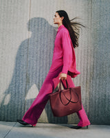 Woman walking with large tote bag in front of textured wall.