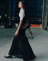 Person walking on a city street carrying a handbag, wearing a long dress.