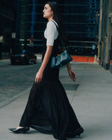 Person walking on a city sidewalk wearing a long dress and carrying a handbag