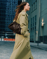 Person walking on city street wearing a long coat and carrying a handbag with a gold chain strap.