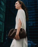 Person in a dress holding a gathered bag, standing outdoors near tall buildings.
