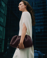 Person in dress holding a gathered handbag, standing in urban setting.
