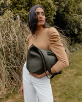 Woman with a bag standing outdoors near tall grass.