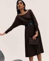 Fashion model in a dress with a belt, holding a clutch bag.