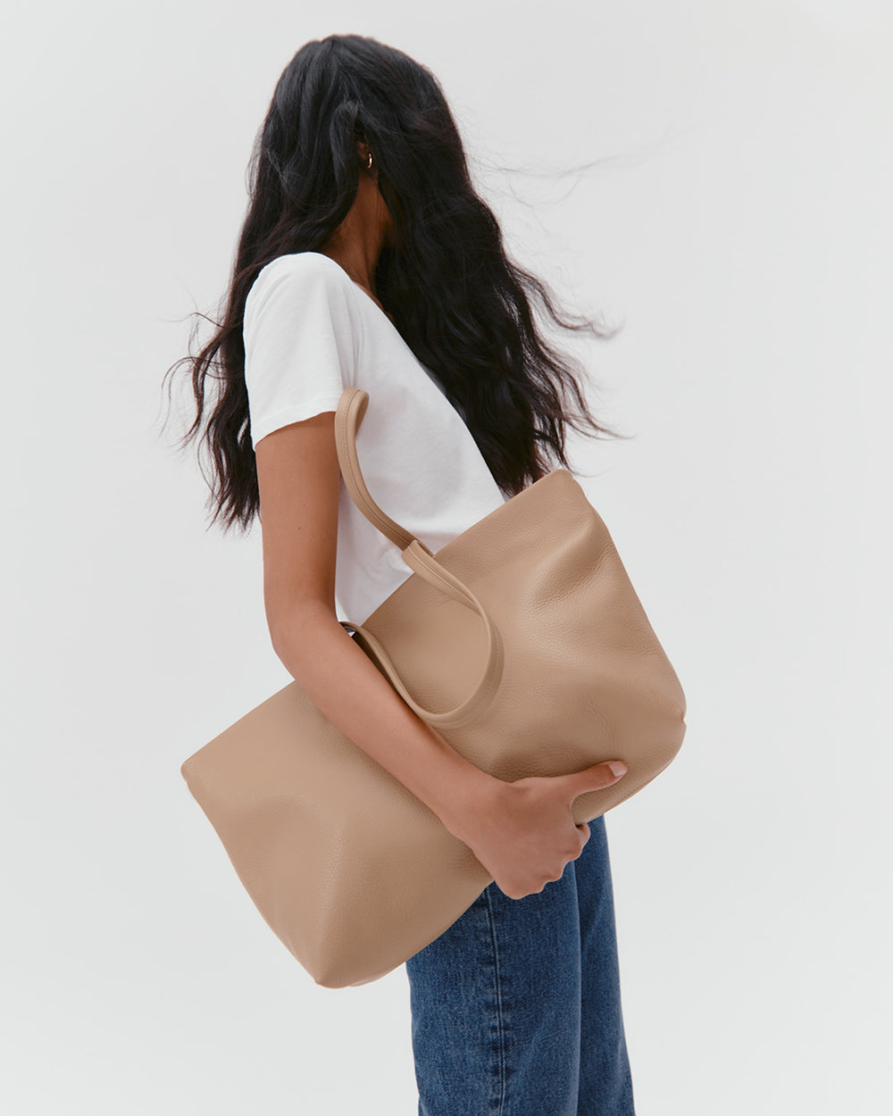 Woman standing sideways holding a large bag over her shoulder.