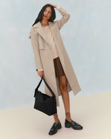 Woman in long coat holding a large shoulder bag, wearing a skirt with loafers and socks