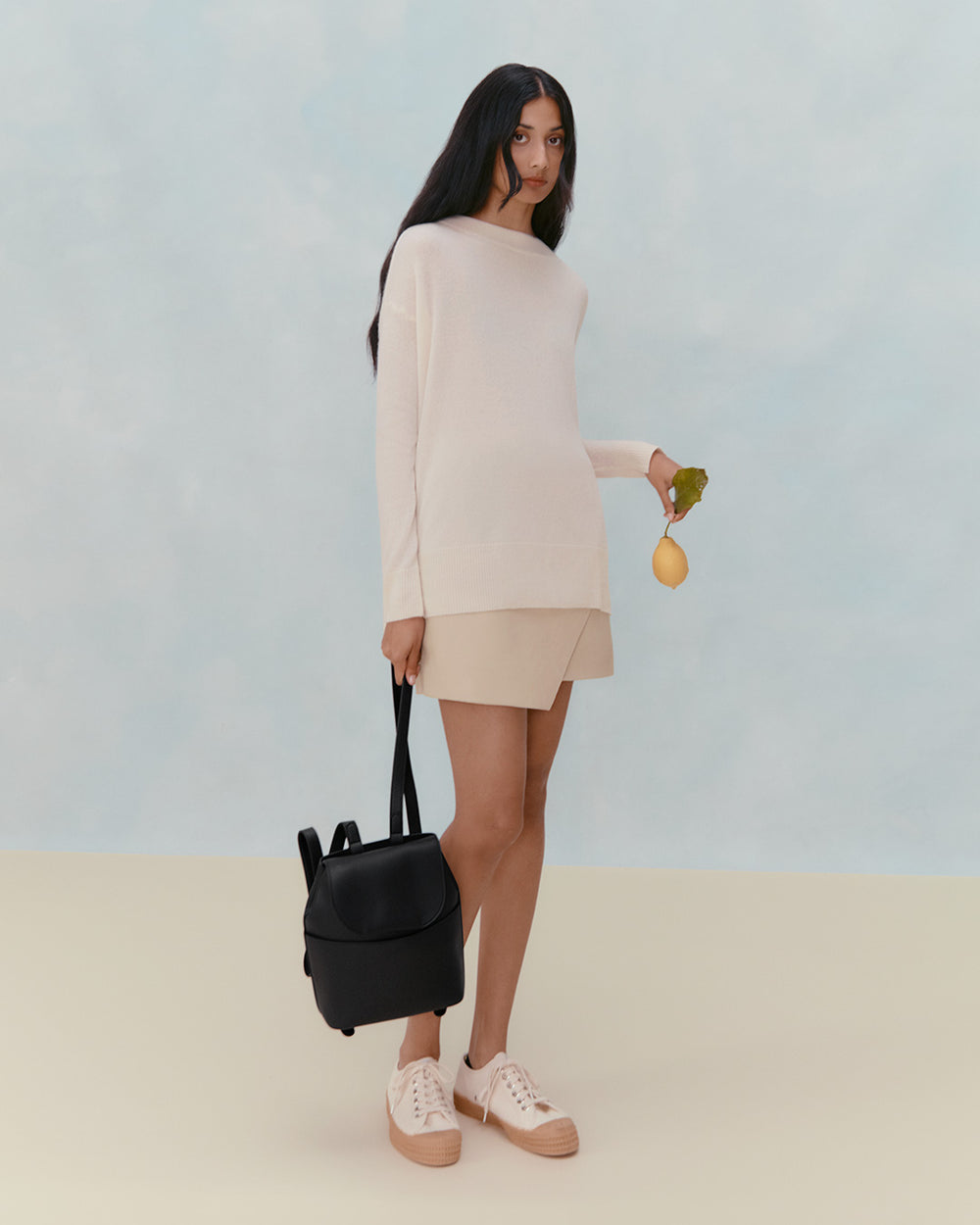 Woman standing, holding purse and a bunch of fresh herbs.