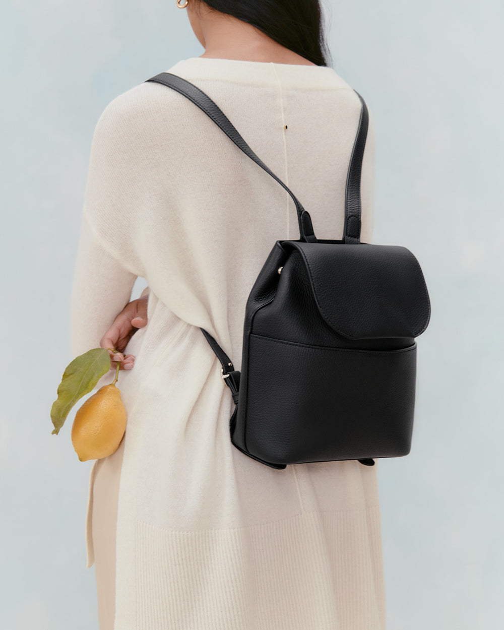 Person with backpack holding a fruit, viewed from behind.