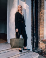 Woman standing on steps with a handbag, near a doorway.