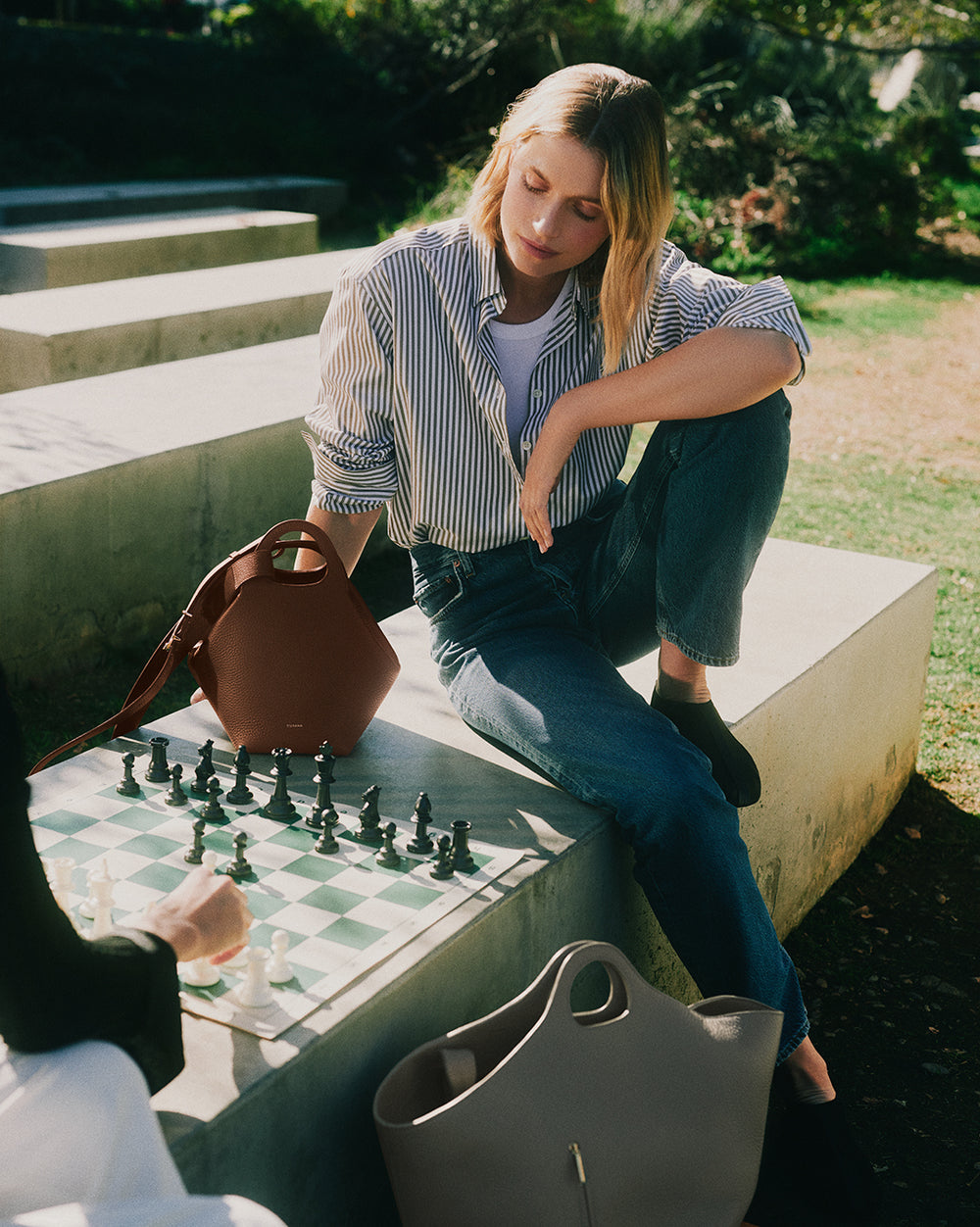Person sitting on steps playing chess with travel bags beside them.