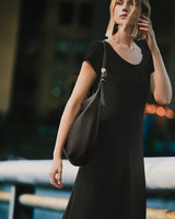 Person in a dress with a shoulder bag against a blurred urban background.