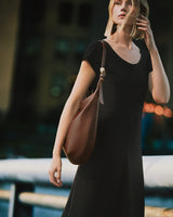 Person in dress holding a shoulder bag outdoors.