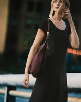Person wearing a dress and carrying a handbag stands outdoors.
