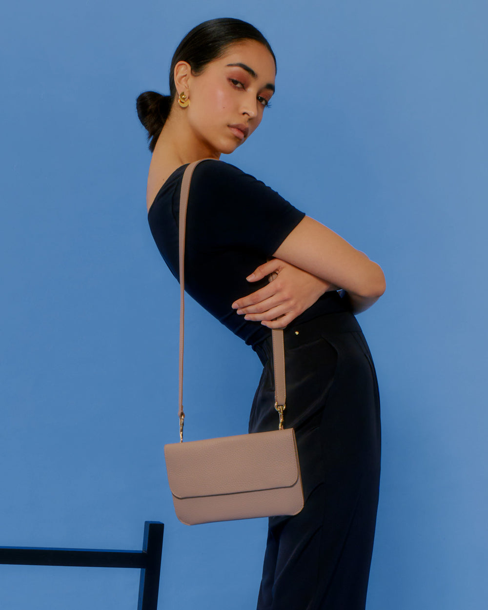 System Flap Bag Person posing with a small shoulder bag against a blue background