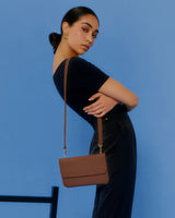 Person posing with shoulder bag against a blue background.