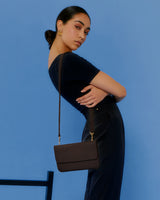 Person posing with a shoulder bag against a plain background.