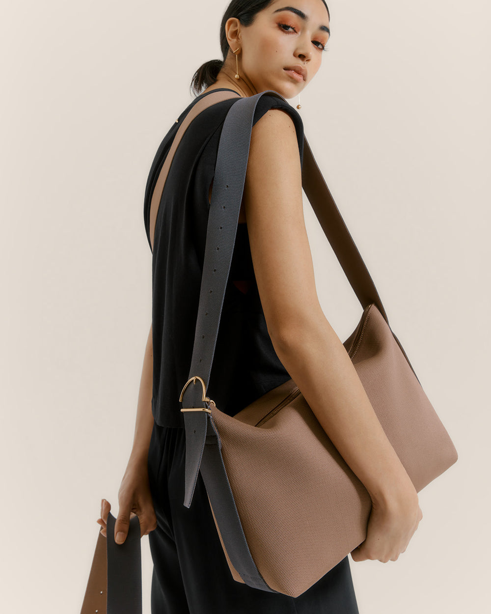 Oversized Sling Bag Person carrying a large shoulder bag over their left shoulder, looking back over their right shoulder