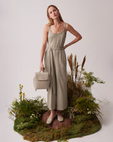 Woman in a dress standing on grass with a bag, surrounded by plants.
