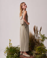 Woman standing on grass patch, wearing a sleeveless top and pants, looking upwards.