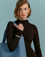 Woman holding a bag over her shoulder and touching the strap.