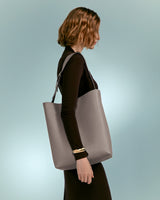 Woman carrying a tote bag, walking, seen from side, head turned away.