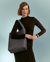 Woman posing with one arm akimbo holding a large bag