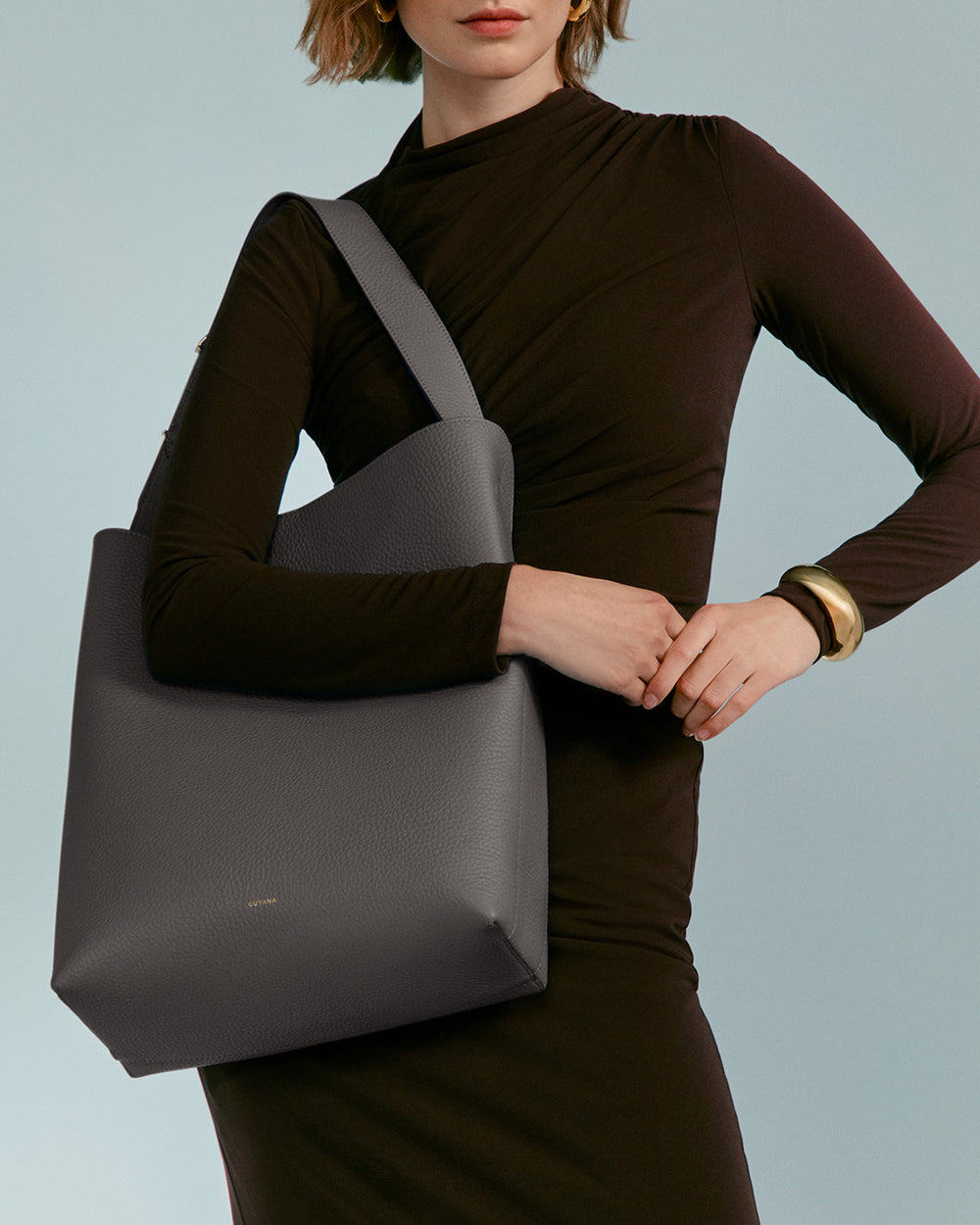 Oversized Linea Bag Person holding a large tote bag against their body while wearing a long-sleeve dress and bracelet.