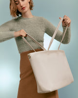 Woman holding a large handbag with two straps.