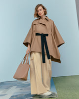 Woman posing in a stylish outfit with a large coat, carrying a tote bag.