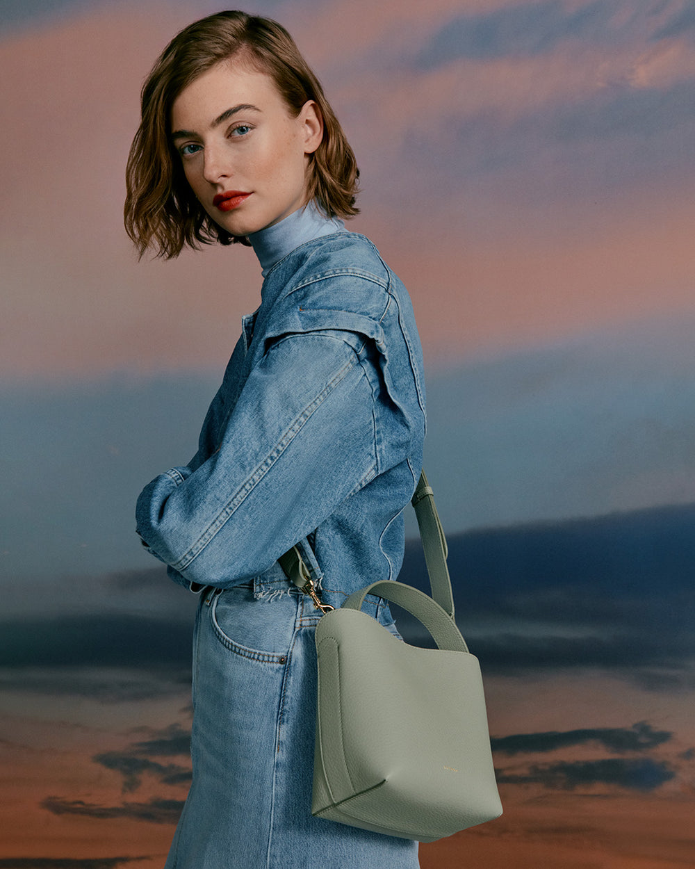 Woman in denim outfit carrying a handbag, looking over shoulder.