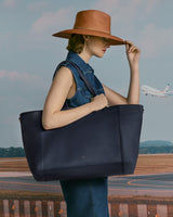 Person in a sleeveless garment holding a large bag with an airplane in the background.